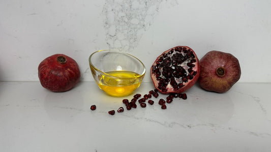 Three pomegranates, a small glass bowl of oil, and some scattered seeds